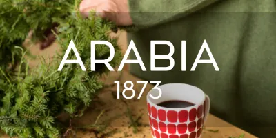 モミの枝を整理する手と、赤と白のドット柄のマグカップ。「ARABIA 1873」の文字がオーバーレイされています。
